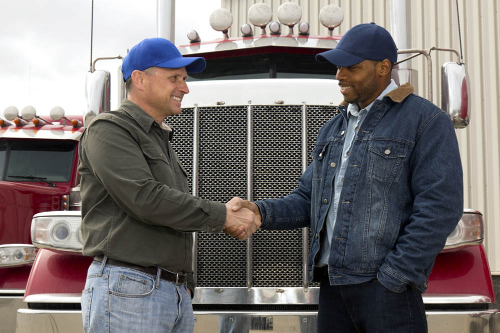 A royalty free image from the trucking industry of two truck drivers shaking hands in front of a semi truck.